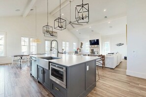 Een ruime keuken met een centraal eiland, moderne apparatuur en hangende verlichting.