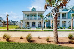 A two-story beachfront house with a balcony, palm trees, and a clear sky. - Palmilla Beach Resort-135 Wild Indigo Street (Port Aransas)
