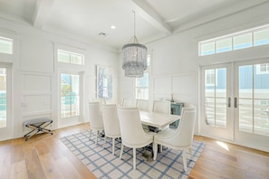 A dining area with a white table and chairs, a chandelier, and a view through large windows. - Palmilla Beach Resort-141 Sunrise Avenue (Port Aransas)