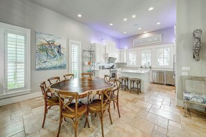 A spacious kitchen with white cabinets, a dining area with a wooden table and chairs, and a large painting on the wall. - Palmilla Beach Resort-145 Sunrise Avenue (Port Aransas)