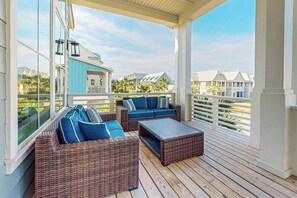 A covered outdoor seating area with wicker furniture and cushions, overlooking a residential area with houses. - Palmilla Beach Resort-147 Sunset Avenue (Port Aransas)