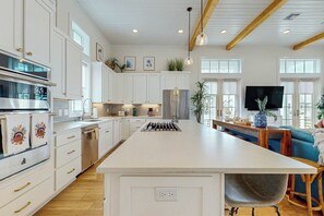 A modern kitchen with white cabinetry, a central island, and a dining area with a blue sofa. - Palmilla Beach Resort-147 Sunset Avenue (Port Aransas)
