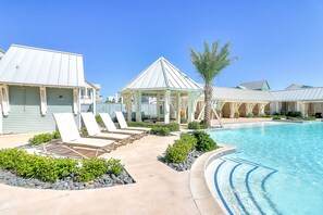 Un espace piscine avec des chaises longues, un kiosque et un ciel d’un bleu éclatant.