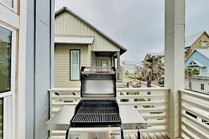Ein Balkon mit Grill, einem weißen Geländer und Blick auf ein Haus mit einem Giebeldach.