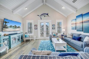 A spacious living room with a high ceiling, a large TV mounted on the wall, a sofa, a coffee table, and a patterned rug. - Palmilla Beach Resort-152 Sea Rocket Lane (Port Aransas)