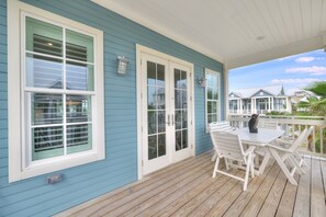 A covered porch with a white table and chairs, a small statue, and a view of neighboring houses. - Palmilla Beach Resort-152 Sea Rocket Lane (Port Aransas)