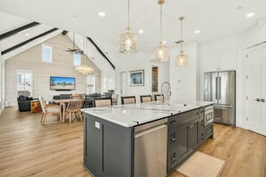Een ruime keuken met een groot eiland, moderne apparatuur en hanglampen.