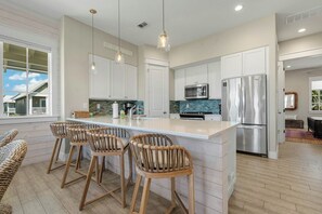 A spacious kitchen with a large island, white cabinetry, stainless steel appliances, and a view of the outside. - Palmilla Beach Resort-158 Sunset Avenue (Port Aransas)