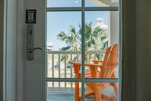 A hotel room with a sliding glass door leading to a balcony with orange chairs and palm trees. - Palmilla Beach Resort-158 Sunset Avenue (Port Aransas)