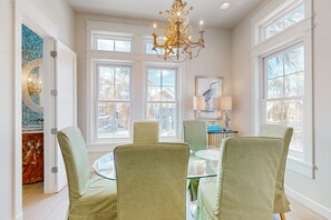 A dining area with a round glass table, green upholstered chairs, and a chandelier. - Palmilla Beach Resort-159 Sunrise Avenue (Port Aransas)