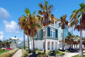 A two-story house with a balcony, surrounded by palm trees and a clear sky. - Palmilla Beach Resort-159 Sunrise Avenue (Port Aransas)