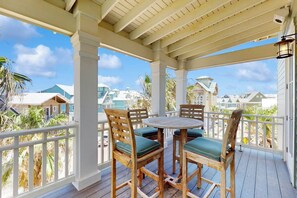 A covered outdoor area with a wooden table and chairs, white railings, and a view of houses in the background. - Palmilla Beach Resort-159 Sunrise Avenue (Port Aransas)