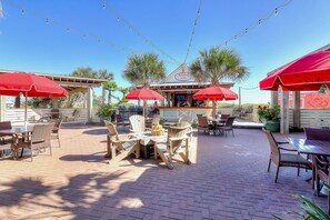 An outdoor patio area with brick flooring, red umbrellas, and outdoor seating. - Palmilla Beach Resort-161 Sunrise Avenue (Port Aransas)