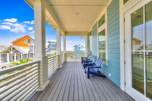A covered porch with wooden flooring and white railings, featuring several blue Adirondack chairs. - Palmilla Beach Resort-161 Sunrise Avenue (Port Aransas)