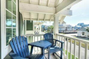 A covered porch with two chairs and a table, overlooking a residential area with houses and a street. - Palmilla Beach Resort-162 Sunset Avenue (Port Aransas)