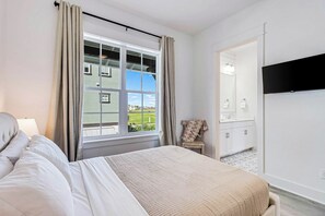 A hotel room with a bed, a window with curtains, a view of a building outside, a bathroom with a mirror, and a flat-screen TV mounted on the wall. - Palmilla Beach Resort-165 Spanish Dagger (Port Aransas)