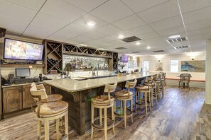 A bar area with a long counter, multiple stools, and a television screen displaying a wrestling event. - Palmilla Beach Resort-165 Spanish Dagger (Port Aransas)
