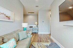 A living room with a sofa, a coffee table, a TV mounted on the wall, and a hallway leading to a kitchen area. - Palmilla Beach Resort-166 Sage Lane (Port Aransas)
