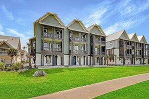 A row of multi-story buildings with balconies, a well-maintained lawn, and a clear sky. - Palmilla Beach Resort-166 Spanish Dagger Lane (Port Aransas)