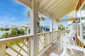 A covered outdoor area with a wooden deck, white chairs, and a view of other buildings. - Palmilla Beach Resort-167 Stargrass Lane (Port Aransas)