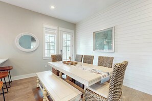A dining area with a white table, patterned chairs, a round mirror, and a framed artwork on the wall. - Palmilla Beach Resort-167 Stargrass Lane (Port Aransas)
