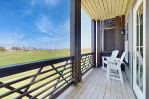 A covered porch with a view of a golf course, two white Adirondack chairs, and a wooden deck. - Palmilla Beach Resort-168 Spanish Dagger Lane (Port Aransas)