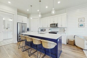 A modern kitchen with white cabinetry, a central island with bar stools, stainless steel appliances, and pendant lighting. - Palmilla Beach Resort-168 Spanish Dagger Lane (Port Aransas)