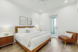 A bedroom with a wooden bed, two bedside tables with lamps, a brown leather sofa, and a door leading to a balcony. - Palmilla Beach Resort-168 Spanish Dagger Lane (Port Aransas)