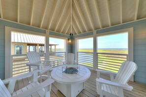 A covered outdoor seating area with Adirondack chairs and a round table, overlooking a coastal landscape. - Palmilla Beach Resort-168 Sunrise Avenue (Port Aransas)