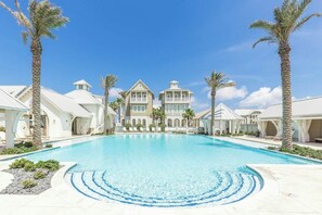 A large swimming pool with a clear blue center, surrounded by palm trees and a multi-story building with balconies. - Palmilla Beach Resort-168 Sunrise Avenue (Port Aransas)