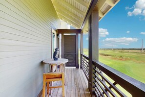 A wooden deck with a table and chair, overlooking a golf course. - Palmilla Beach Resort-170 Spanish Dagger Lane (Port Aransas)