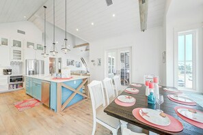 A spacious kitchen with a central island, white cabinetry, and a dining area with a wooden table set for four. - Palmilla Beach Resort-171 Sunrise Avenue (Port Aransas)