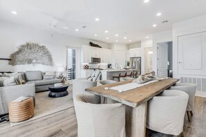 Une cuisine moderne avec des meubles blancs, un îlot central et un coin repas comprenant une table et des chaises en bois.