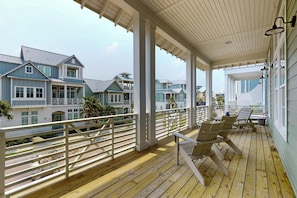 A covered porch with wooden flooring and white railings, overlooking a row of houses with multiple stories and balconies. - Palmilla Beach Resort-172 Sunrise Avenue (Port Aransas)