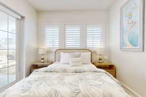 Een slaapkamer met een bed, twee nachtkastjes, een raam met jaloezieën en een schilderij aan de muur.