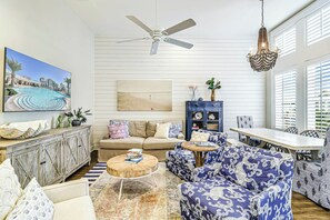 A living room with a ceiling fan, a dining area with a table and chairs, a sofa set, a cabinet, and a large framed picture on the wall. - Palmilla Beach Resort-177 Sunset Avenue (Port Aransas)