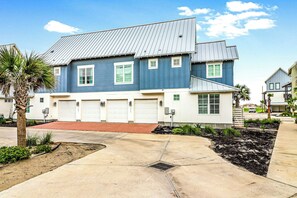 A two-story residential building with a blue exterior, white garage doors, and a sloped metal roof. - Palmilla Beach Resort-177 Sunset Avenue (Port Aransas)