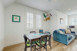A dining area with a table and chairs, a blue sofa, and a kitchen area with a microwave. - Palmilla Beach Resort-182 Sage Lane (Port Aransas)