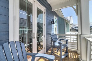 En overdækket veranda med Adirondack-stole, en glasdør indgang og udsigt til nabohusene.