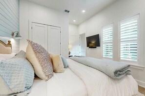 A bedroom with a bed, pillows, a TV, and a window with blinds. - Palmilla Beach Resort-183 Stargrass Lane (Port Aransas)