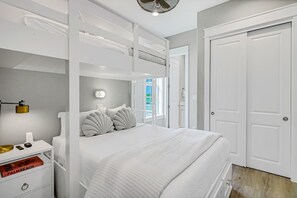 A bedroom with a bunk bed, a bedside table with a lamp, a book, and a door to the right. - Palmilla Beach Resort-184 Sunset Avenue (Port Aransas)
