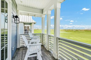 A covered porch with white Adirondack chairs, a small building, and a view of a golf course. - Palmilla Beach Resort-184 Sunset Avenue (Port Aransas)