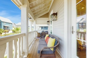 A covered porch with a seating area, wooden railings, and a view of adjacent buildings. - Palmilla Beach Resort-185 Sunset Avenue (Port Aransas)