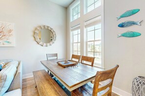 A dining area with a wooden table, chairs, a bench, and a large window. - Palmilla Beach Resort-185 Sunset Avenue (Port Aransas)