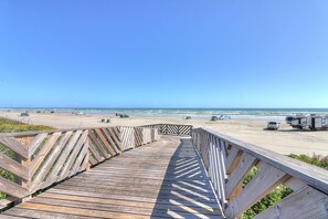 A wooden boardwalk leading to a beach with vehicles and a clear sky. - Palmilla Beach Resort-186 Sunrise Avenue (Port Aransas)