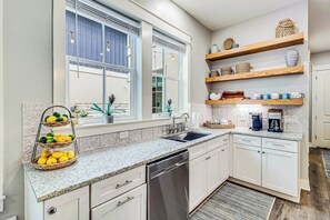 A modern kitchen with white cabinetry, a granite countertop, a built-in dishwasher, and a coffee maker. - Palmilla Beach Resort-187 Stargrass Lane (Port Aransas)