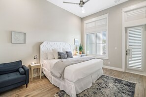 A bedroom with a bed, bedside table, lamp, chair, and a window with blinds. - Palmilla Beach Resort-187 Stargrass Lane (Port Aransas)