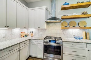 A kitchen with white cabinets, a stainless steel stove, and decorative items on shelves. - Palmilla Beach Resort-187 Stargrass Lane (Port Aransas)