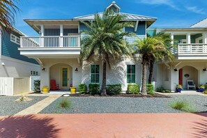 A two-story house with a balcony, a front door, and a small garden area with palm trees. - Palmilla Beach Resort-191 Stargrass Lane (Port Aransas)