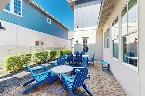 A patio with blue Adirondack chairs and a round table, surrounded by a white fence and greenery. - Palmilla Beach Resort-191 Stargrass Lane (Port Aransas)